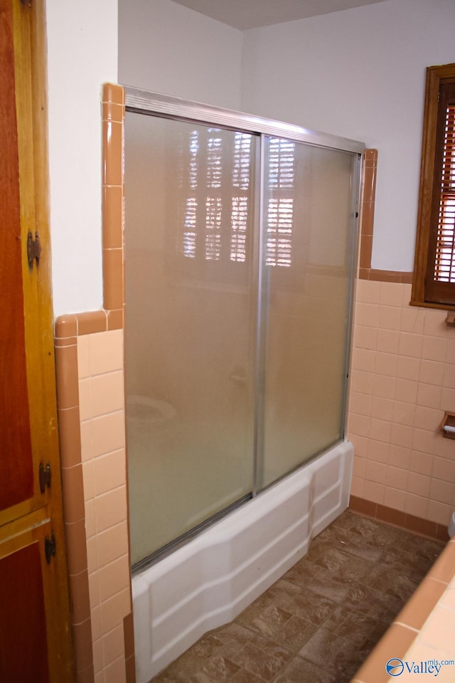 bathroom featuring combined bath / shower with glass door and tile walls