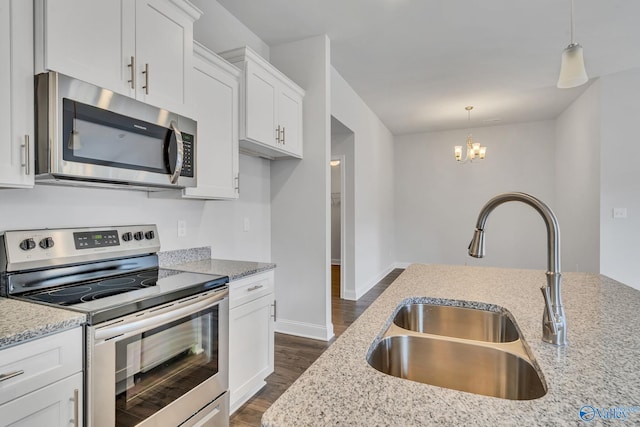 kitchen featuring white cabinets, light stone counters, hanging light fixtures, stainless steel appliances, and a sink