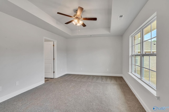 carpeted empty room with baseboards, visible vents, a tray ceiling, and a ceiling fan