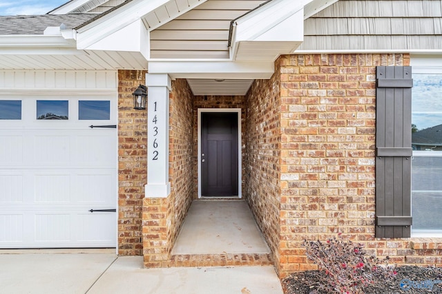 view of exterior entry with brick siding, roof with shingles, and an attached garage