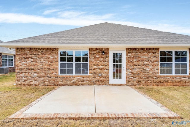 rear view of house featuring a patio, central AC unit, brick siding, a shingled roof, and a lawn