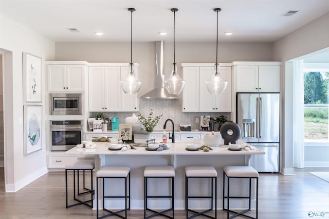 kitchen with stainless steel appliances, a kitchen bar, a center island with sink, and white cabinets