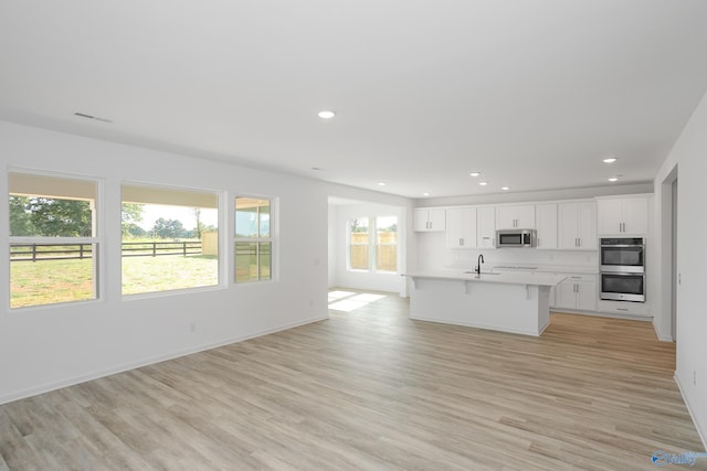 kitchen featuring an island with sink, white cabinets, a kitchen bar, stainless steel appliances, and light wood-type flooring