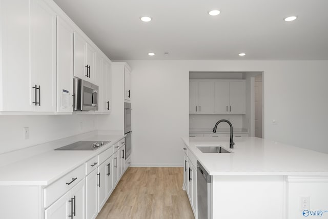 kitchen featuring appliances with stainless steel finishes, sink, white cabinets, a kitchen island with sink, and light wood-type flooring