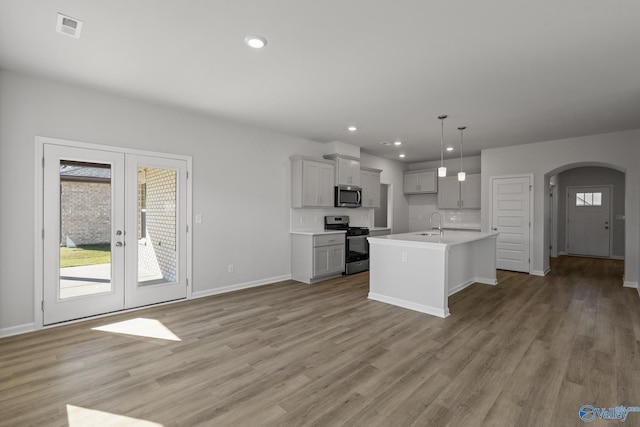 kitchen featuring hanging light fixtures, french doors, appliances with stainless steel finishes, gray cabinets, and an island with sink