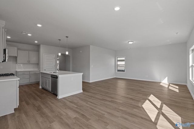 kitchen with dishwasher, hanging light fixtures, decorative backsplash, sink, and a center island with sink