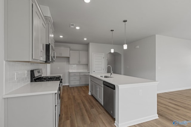 kitchen featuring sink, backsplash, appliances with stainless steel finishes, and a center island with sink