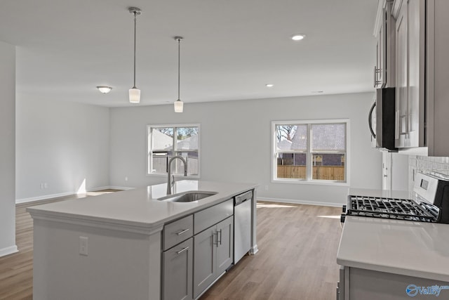 kitchen featuring appliances with stainless steel finishes, a kitchen island with sink, gray cabinetry, sink, and pendant lighting