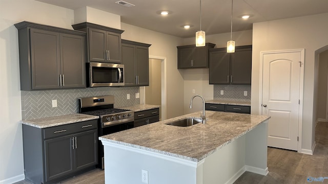 kitchen with light stone counters, sink, appliances with stainless steel finishes, and a center island with sink