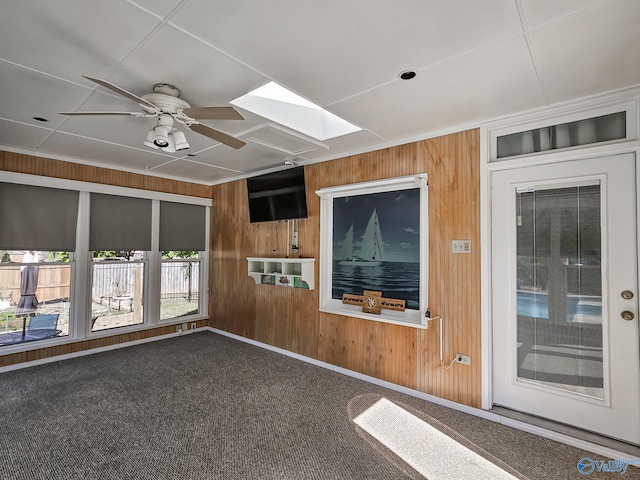 unfurnished living room featuring carpet, wood walls, a skylight, and ceiling fan