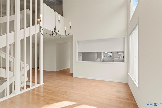 unfurnished living room with a notable chandelier, wood-type flooring, and a high ceiling