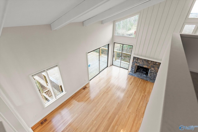 unfurnished living room with a stone fireplace, wood-type flooring, high vaulted ceiling, and beamed ceiling