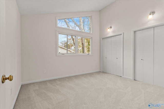 unfurnished bedroom with multiple closets, light carpet, and a high ceiling