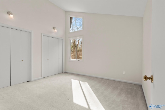 unfurnished bedroom with light carpet, high vaulted ceiling, and multiple closets