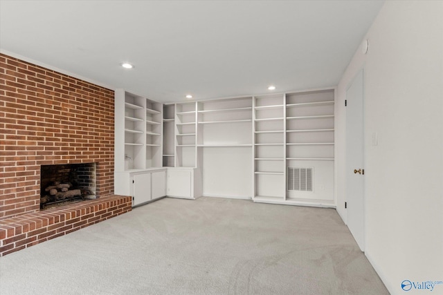 unfurnished living room featuring a brick fireplace, built in shelves, and light colored carpet