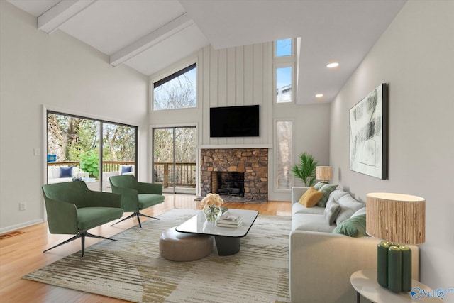 living room featuring high vaulted ceiling, beam ceiling, hardwood / wood-style floors, and a stone fireplace