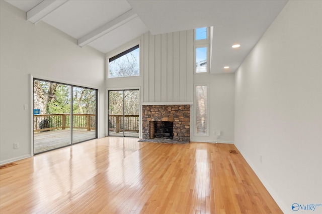 unfurnished living room featuring a stone fireplace, high vaulted ceiling, beam ceiling, and light hardwood / wood-style flooring