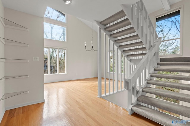 stairs featuring a towering ceiling, hardwood / wood-style floors, and a notable chandelier