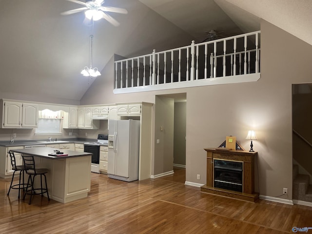 kitchen with a kitchen breakfast bar, white appliances, ceiling fan with notable chandelier, high vaulted ceiling, and a kitchen island