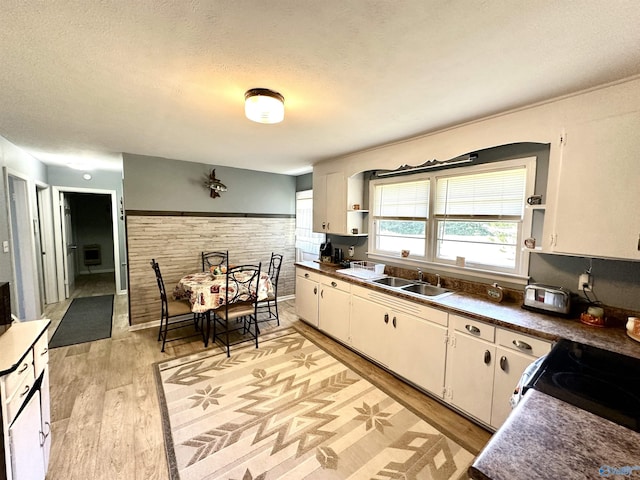 kitchen featuring wainscoting, light wood-style flooring, a textured ceiling, open shelves, and a sink