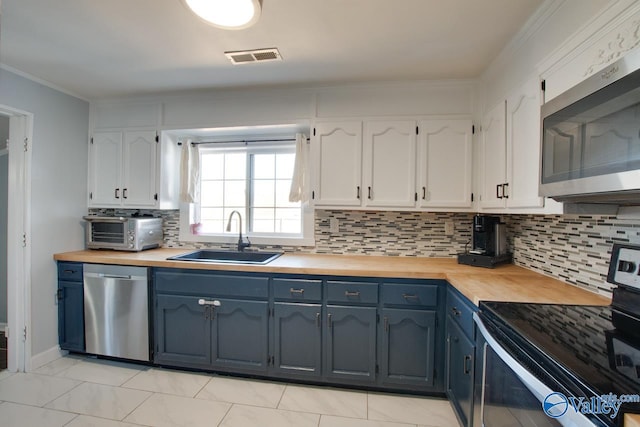 kitchen featuring white cabinets, stainless steel appliances, wood counters, and a sink