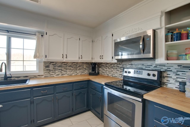 kitchen with wooden counters, a sink, stainless steel appliances, white cabinets, and crown molding