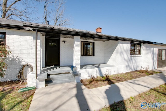 property entrance featuring metal roof, brick siding, a porch, and a chimney