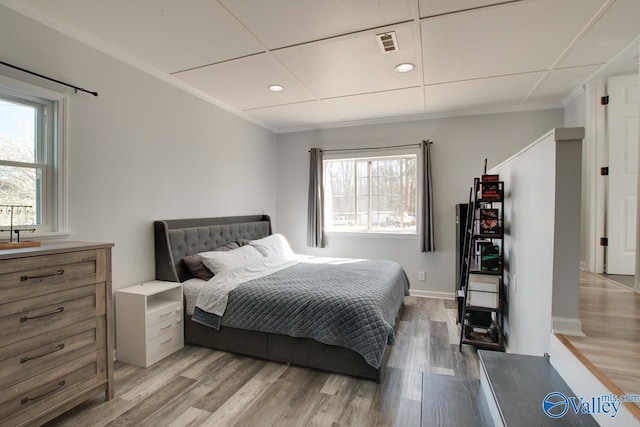 bedroom featuring multiple windows, crown molding, and light wood-style flooring