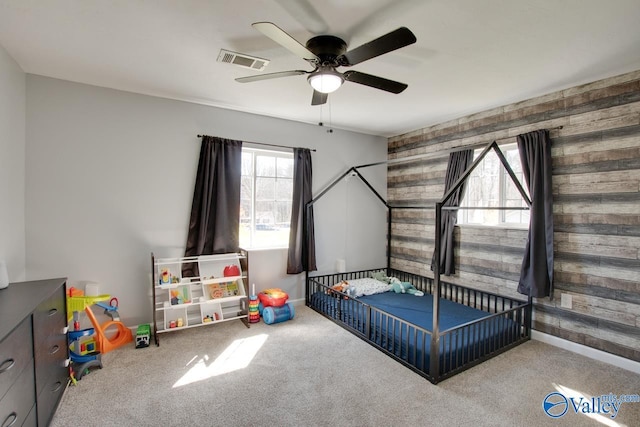 bedroom with visible vents, wood walls, a ceiling fan, and carpet