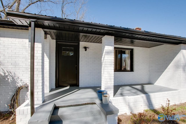 view of exterior entry with a porch and brick siding