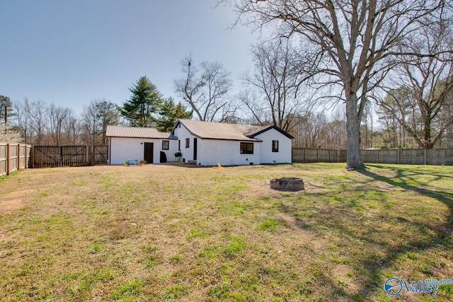 exterior space with metal roof, a yard, a fenced backyard, and a fire pit