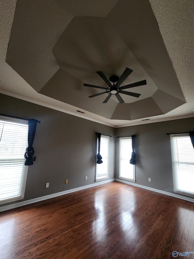 empty room with crown molding, a ceiling fan, wood finished floors, a raised ceiling, and visible vents