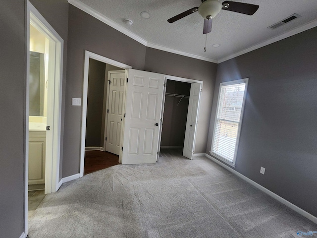 unfurnished bedroom with a textured ceiling, carpet floors, baseboards, ornamental molding, and visible vents