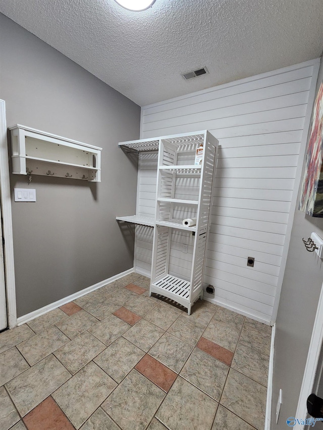 clothes washing area with a textured ceiling, visible vents, and baseboards