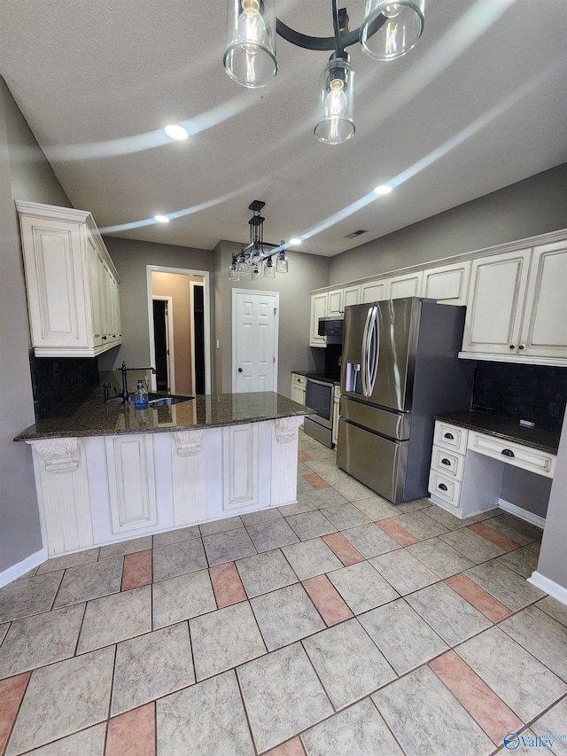 kitchen with a peninsula, dark stone counters, white cabinetry, decorative backsplash, and appliances with stainless steel finishes