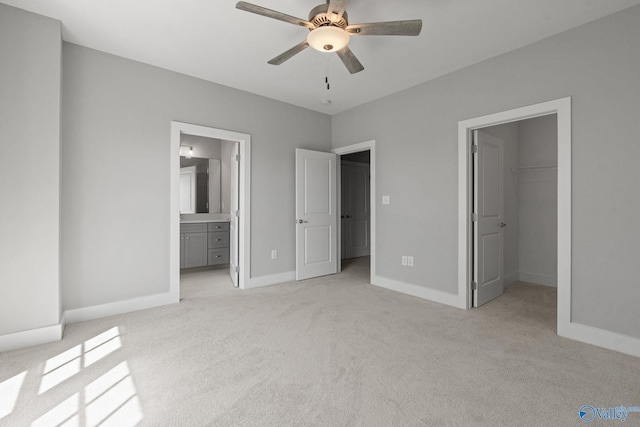 unfurnished bedroom featuring light carpet, ensuite bathroom, ceiling fan, and a walk in closet