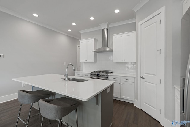 kitchen featuring an island with sink, sink, wall chimney exhaust hood, white cabinetry, and stainless steel appliances