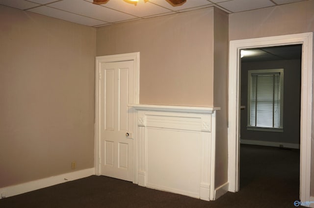 interior space featuring dark colored carpet, a paneled ceiling, and baseboards