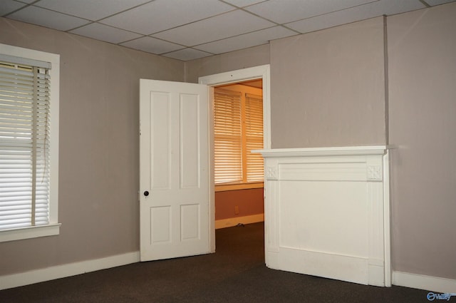 unfurnished bedroom with a paneled ceiling, baseboards, and dark carpet