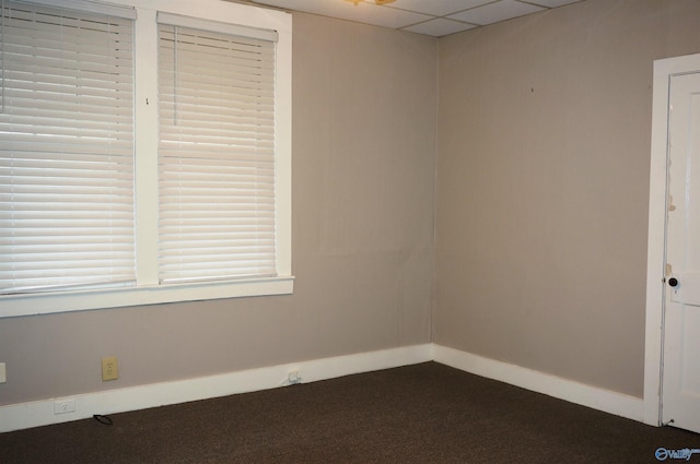 unfurnished room with a paneled ceiling, dark carpet, and baseboards