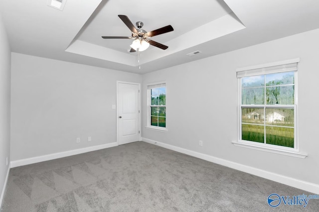 carpeted spare room featuring a tray ceiling and ceiling fan