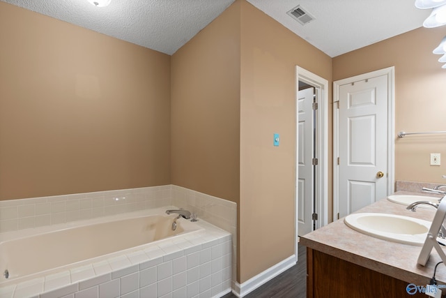 full bathroom featuring a sink, a textured ceiling, visible vents, and a bath