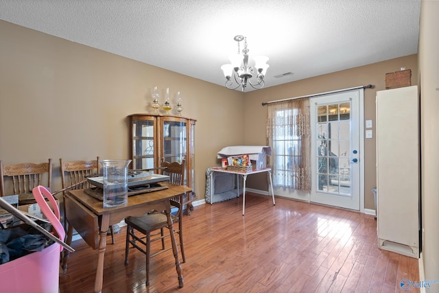 dining area featuring a textured ceiling, visible vents, wood finished floors, and an inviting chandelier