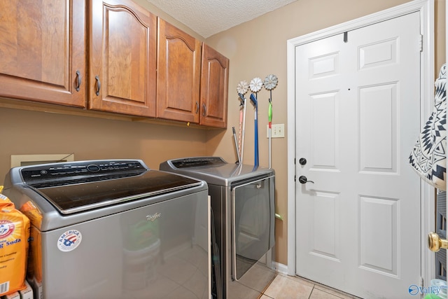 laundry area with a textured ceiling, washer and dryer, cabinet space, and light tile patterned floors