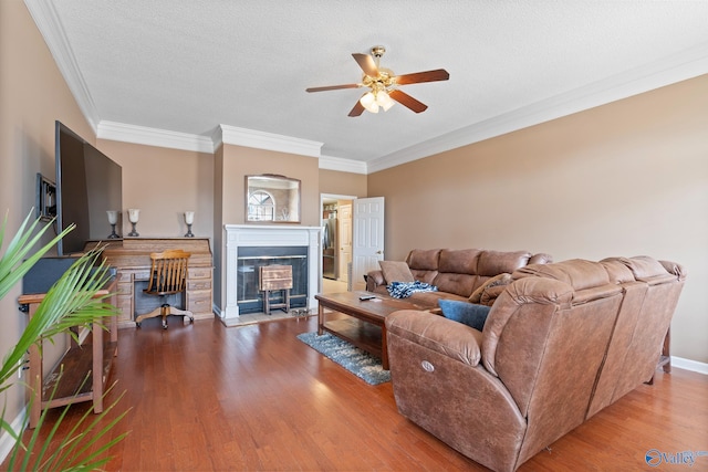 living area with crown molding, a textured ceiling, a ceiling fan, a glass covered fireplace, and wood finished floors