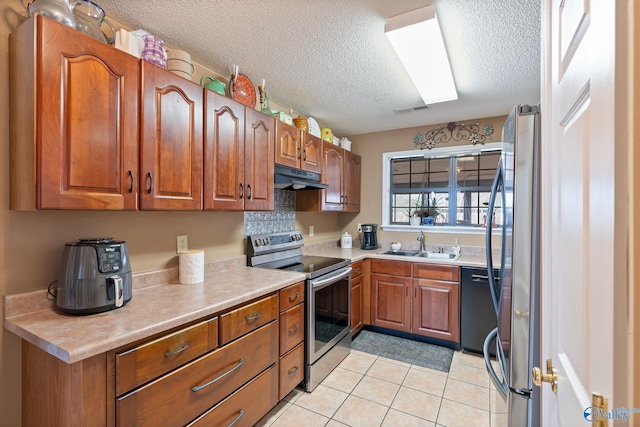 kitchen featuring brown cabinetry, under cabinet range hood, a sink, and stainless steel appliances