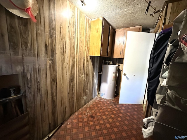washroom with water heater, tile patterned floors, wooden walls, and a textured ceiling