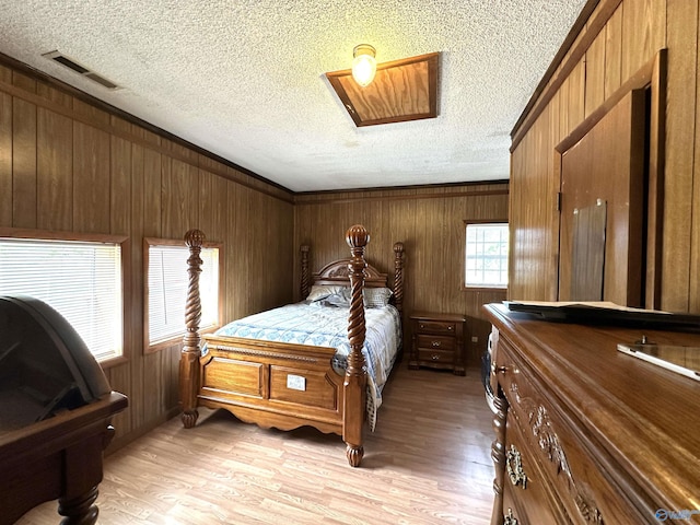 bedroom with a textured ceiling, visible vents, wood walls, and light wood-type flooring