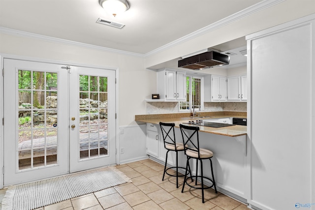 kitchen featuring a sink, visible vents, white cabinets, a kitchen bar, and crown molding