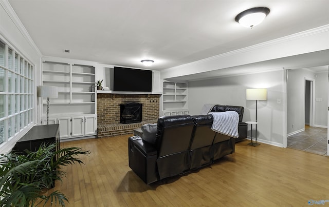 living room with ornamental molding, a brick fireplace, built in shelves, and light wood-style floors